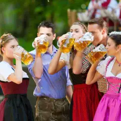 Cinco amigos brindan con jarras de cerveza, celebrando cuando es Oktoberfest con trajes bávaros tradicionales.