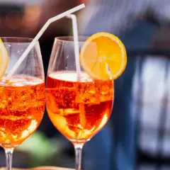 Dos Aperol Spritz refrescantes, con rodajas de naranja y pajitas, evocan el aperitivo italiano y su aperol spritz origen.