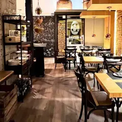 Interior de un bistro bar con mesas puestas, sillas de madera oscura y decoración industrial.