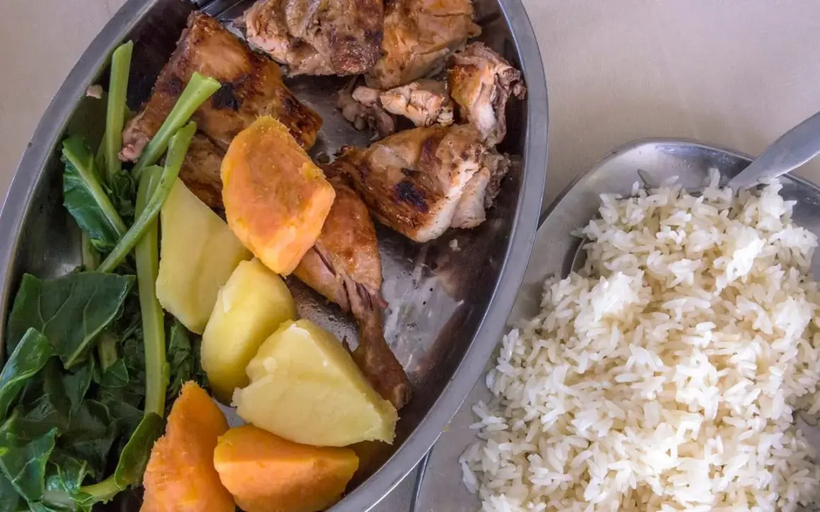 Sabrosa comida de Gambia: pollo asado, batatas, patatas y verduras verdes, acompañado de arroz blanco.