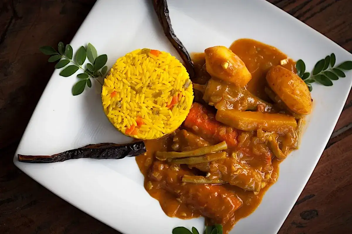 Delicioso plato de comida de Gambia: arroz amarillo con verduras y un guiso de carne con patatas y zanahorias.